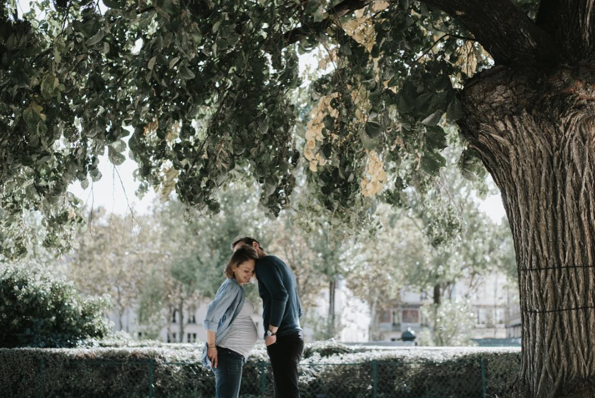 photographie d'un couple qui attend un enfant avec la grossesse de la maman sous un arbre dans les rues de Paris