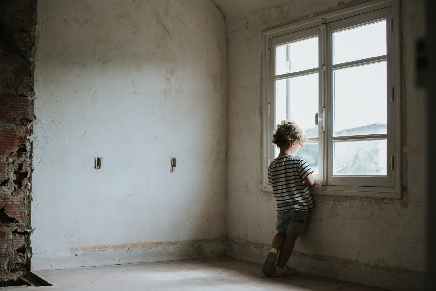 petit garçon qui regarde par la fenêtre au loin prise en photo par Candice Henin photographe de famille naturel à paris